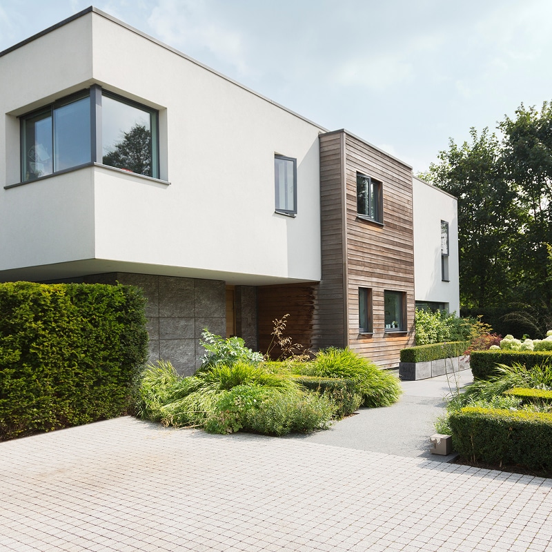 Villa moderne blanc et bois avec grandes baies vitrées, allée pavée et aménagement paysager luxuriant.